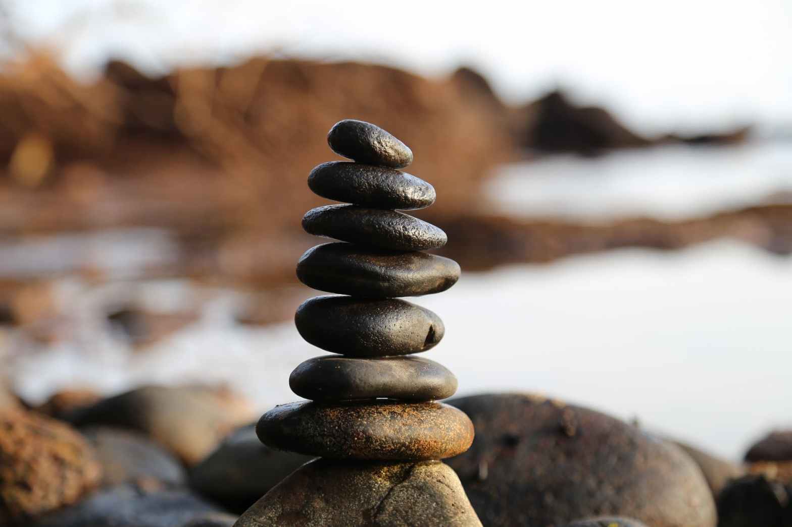 An image of a blurred rocky shore with a focus on 8 small pebbles stacked on each other.